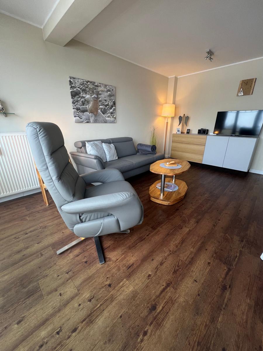 Wohnzimmer mit grauem Sofa, bequemer Sessel und Holztisch.