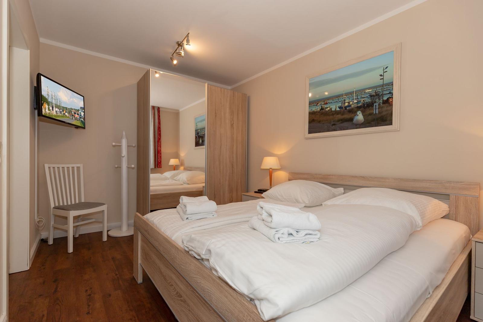 Schlafzimmer mit Doppelbett, Fernseher und Spiegel. Holzboden und Wandbild mit Hafenmotiv.