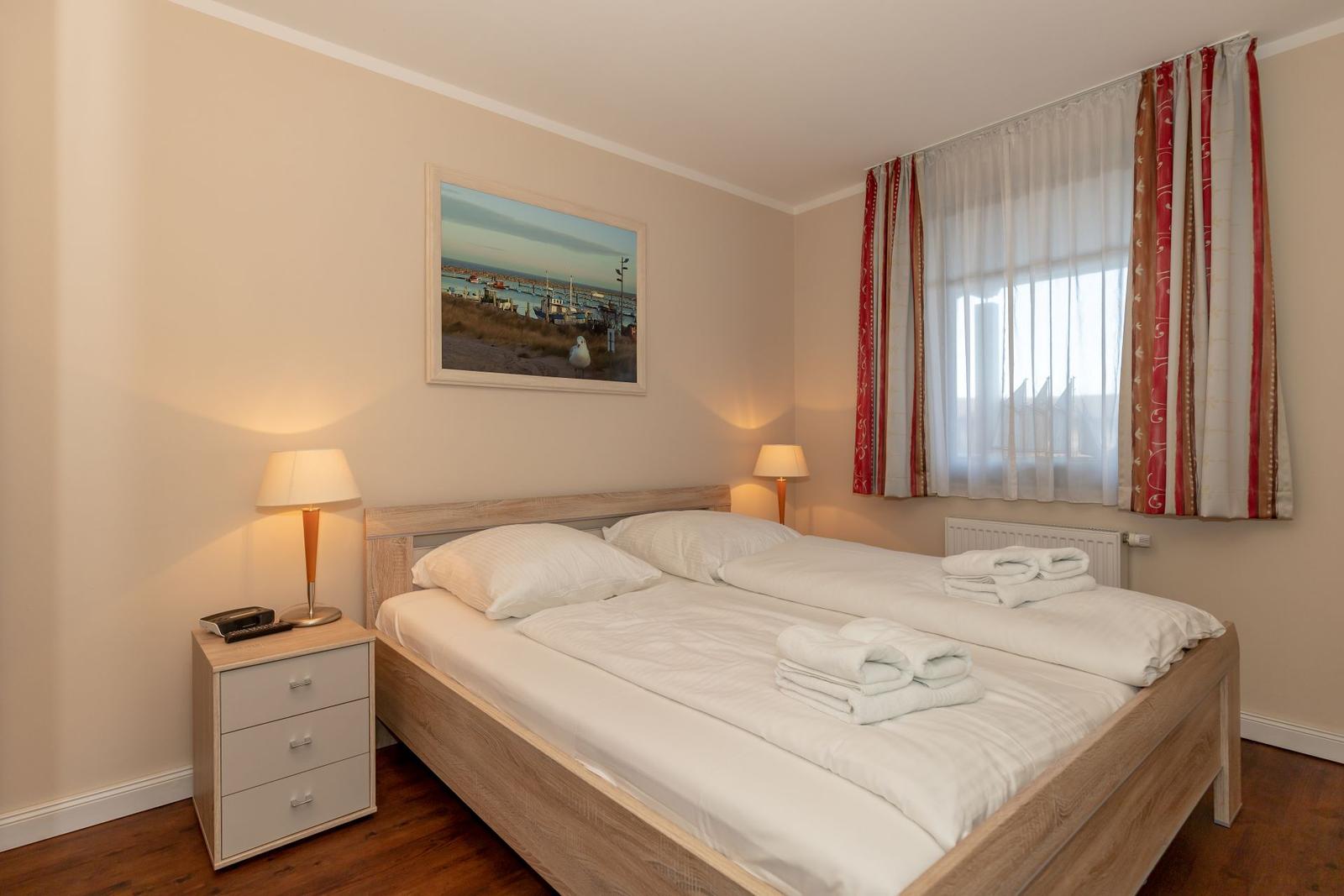 Schlafzimmer mit Doppelbett, Nachttisch und Fenster mit Vorhängen.