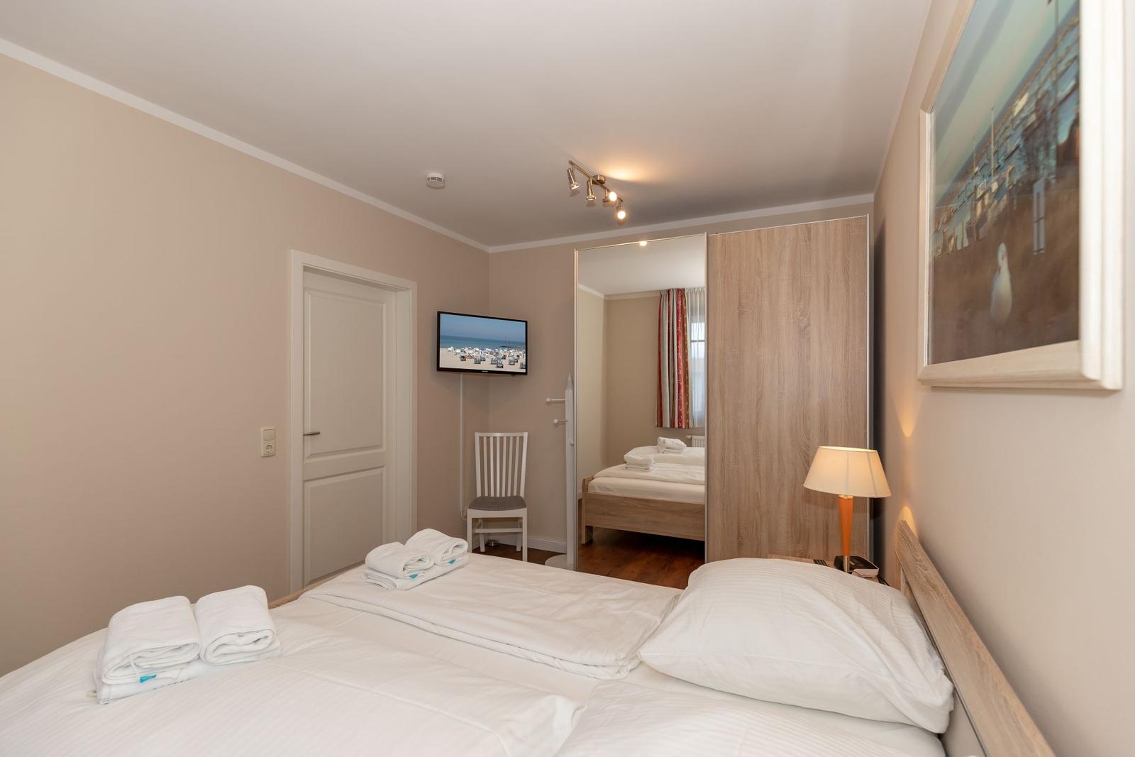 Schlafzimmer mit Bett, TV und Spiegeltüren. Handtuch auf Bett.