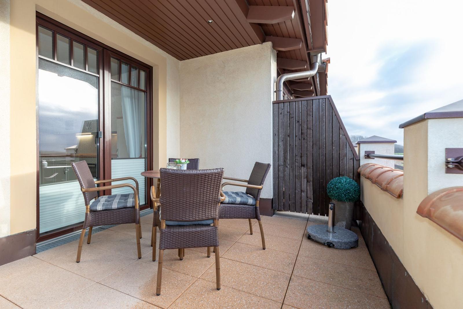 Terrasse mit Tisch und vier Stühlen, Glasfront und Holzgeländer.