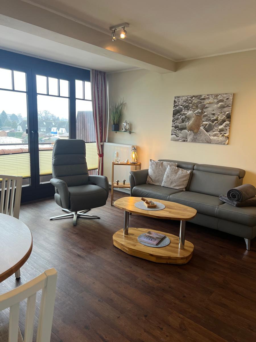 Wohnzimmer mit Sofa, Sessel und Holztisch. Große Fensterfront mit Blick.