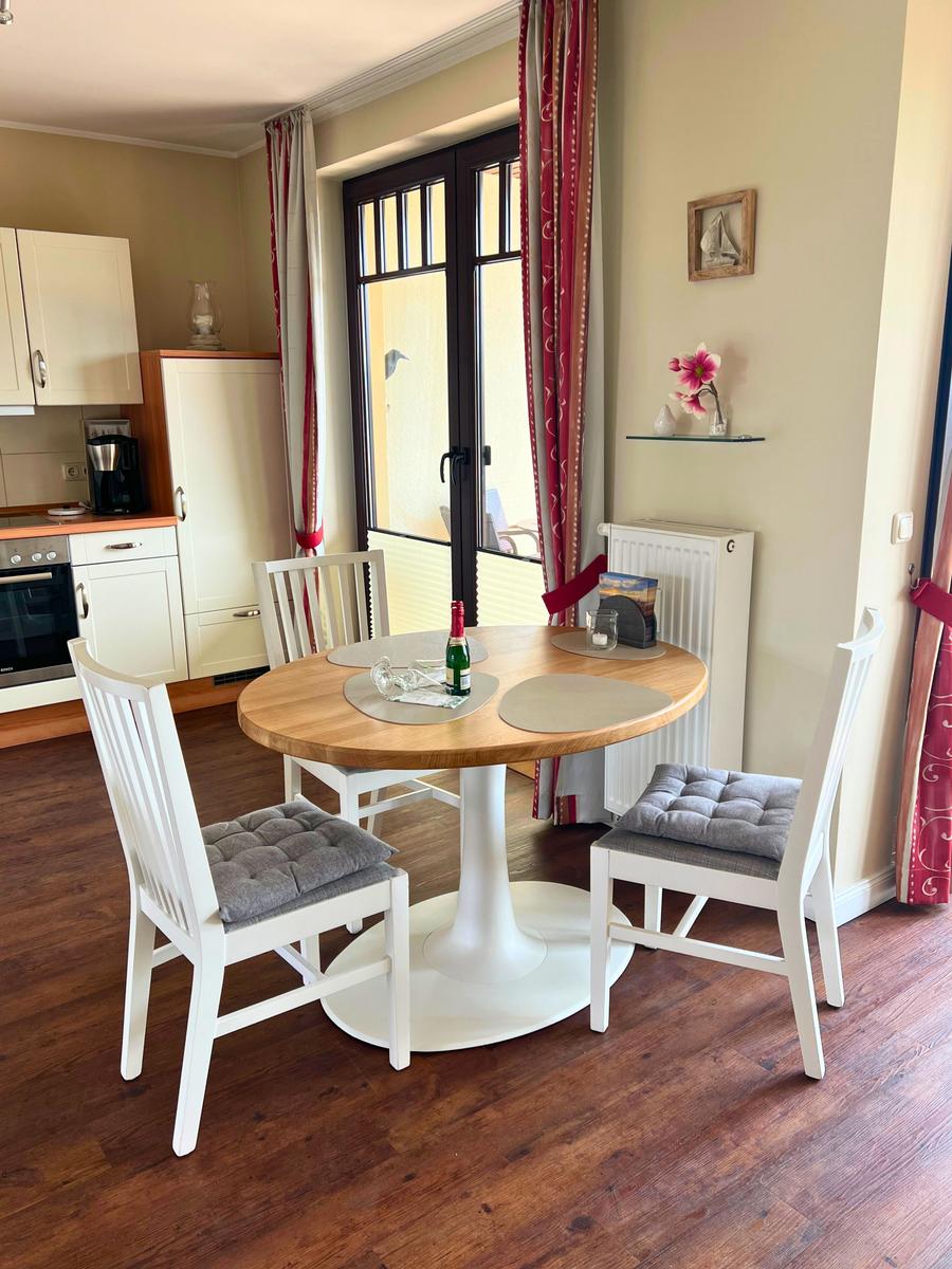 Rundes Esszimmer mit Tisch und Stühlen, Küchenbereich und Fenster zur Terrasse.