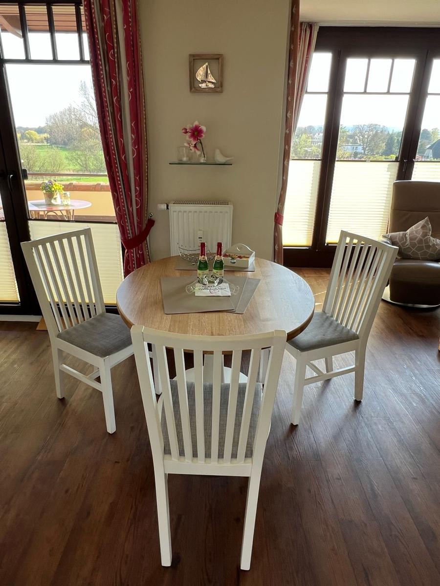 Runder Tisch mit drei Stühlen, Blick auf Terrasse und Landschaft.