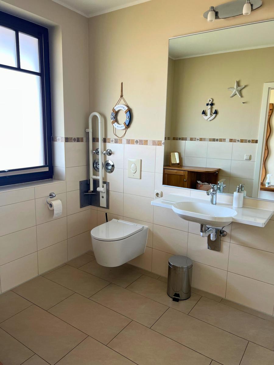 Badezimmer mit WC, Waschbecken und Fenster. Wandgestaltung mit Segel- und Ankermotiven.