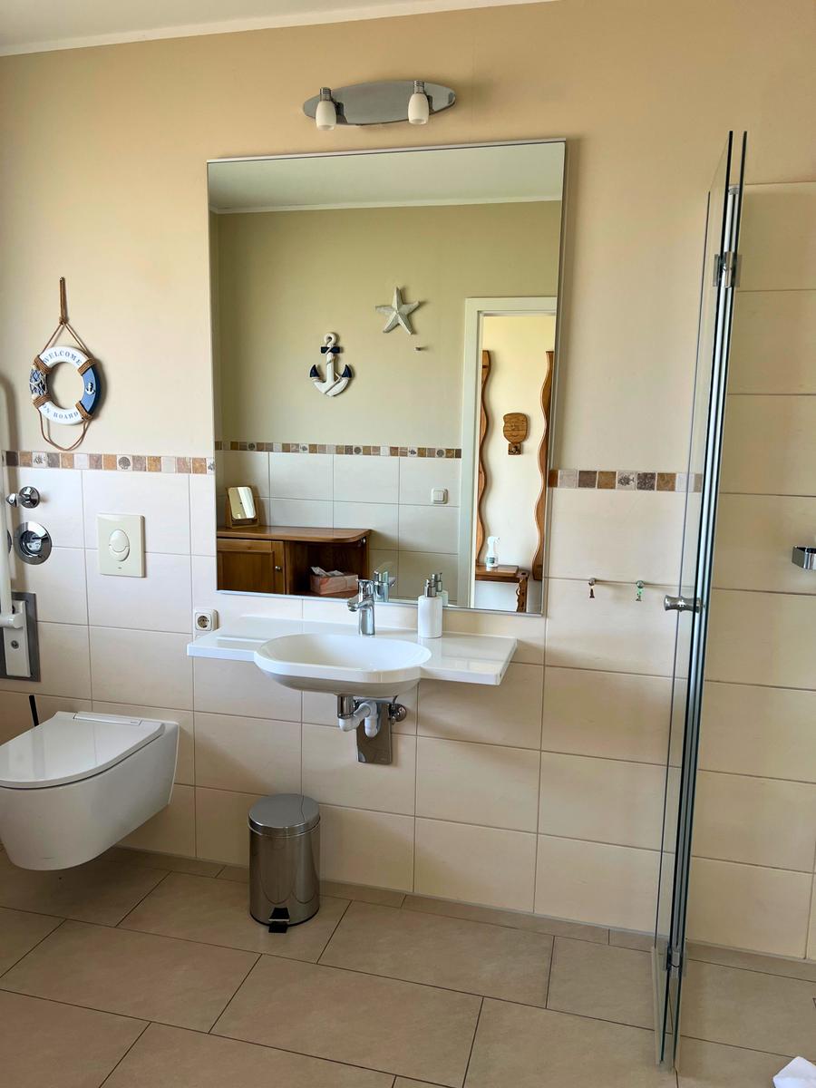 Badezimmer mit Spiegel, Waschbecken, Toilette und Dusche. Wanddekoration mit Anker und Stern.
