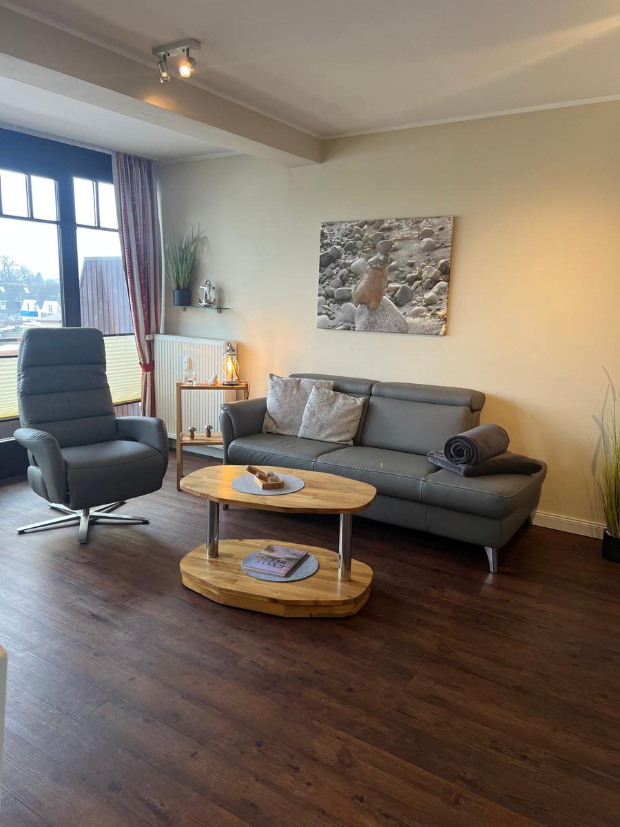 Wohnzimmer mit grauem Sofa, Sessel und Holztisch. Fenster, Wandbild und Holzboden.