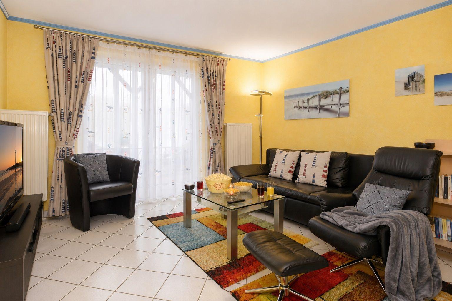 Wohnzimmer mit Sofa, Sessel, Glas-Tisch und Fernseher an Wand