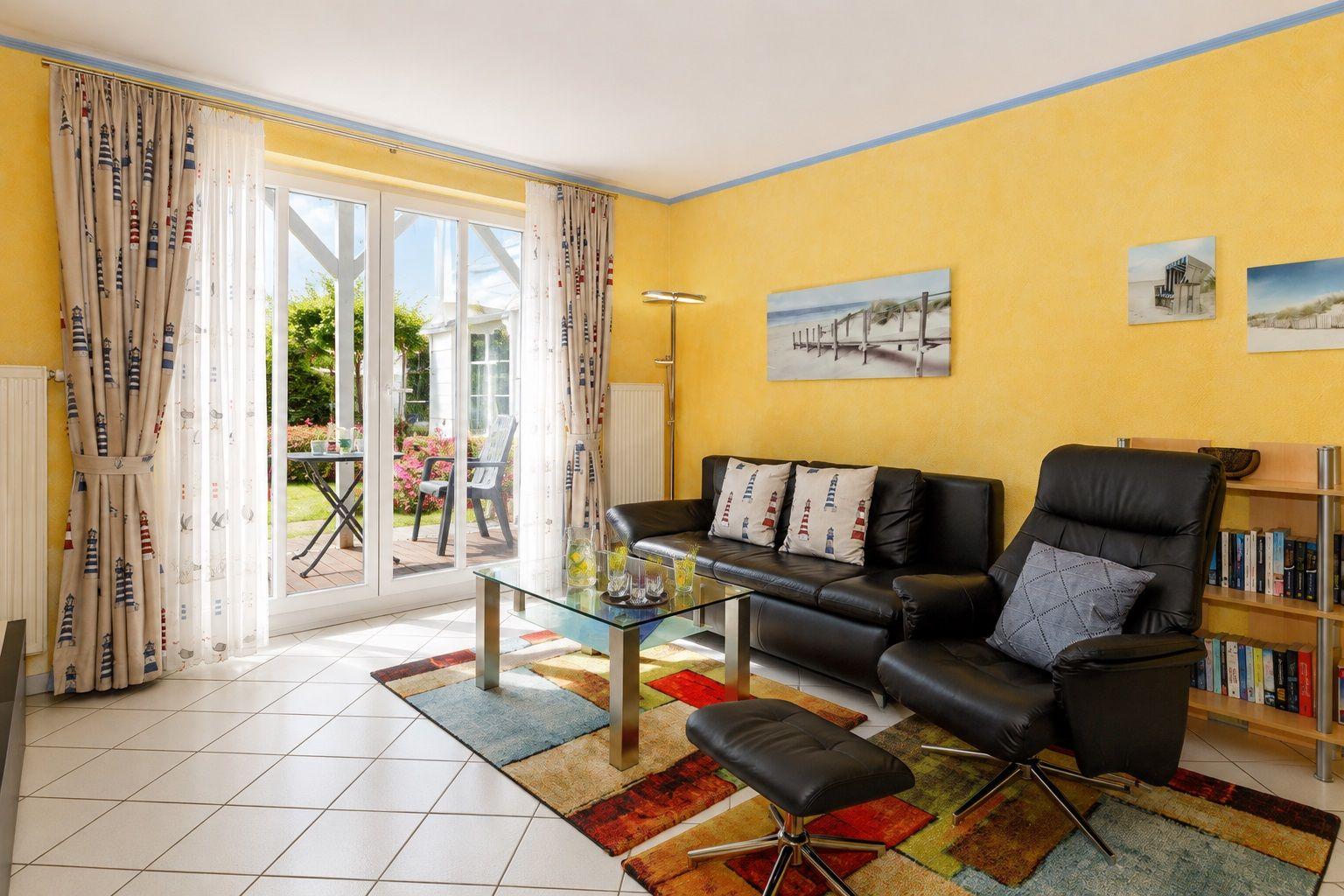 Wohnzimmer mit Sofa, Sessel, Fernseher und Terrassentür.