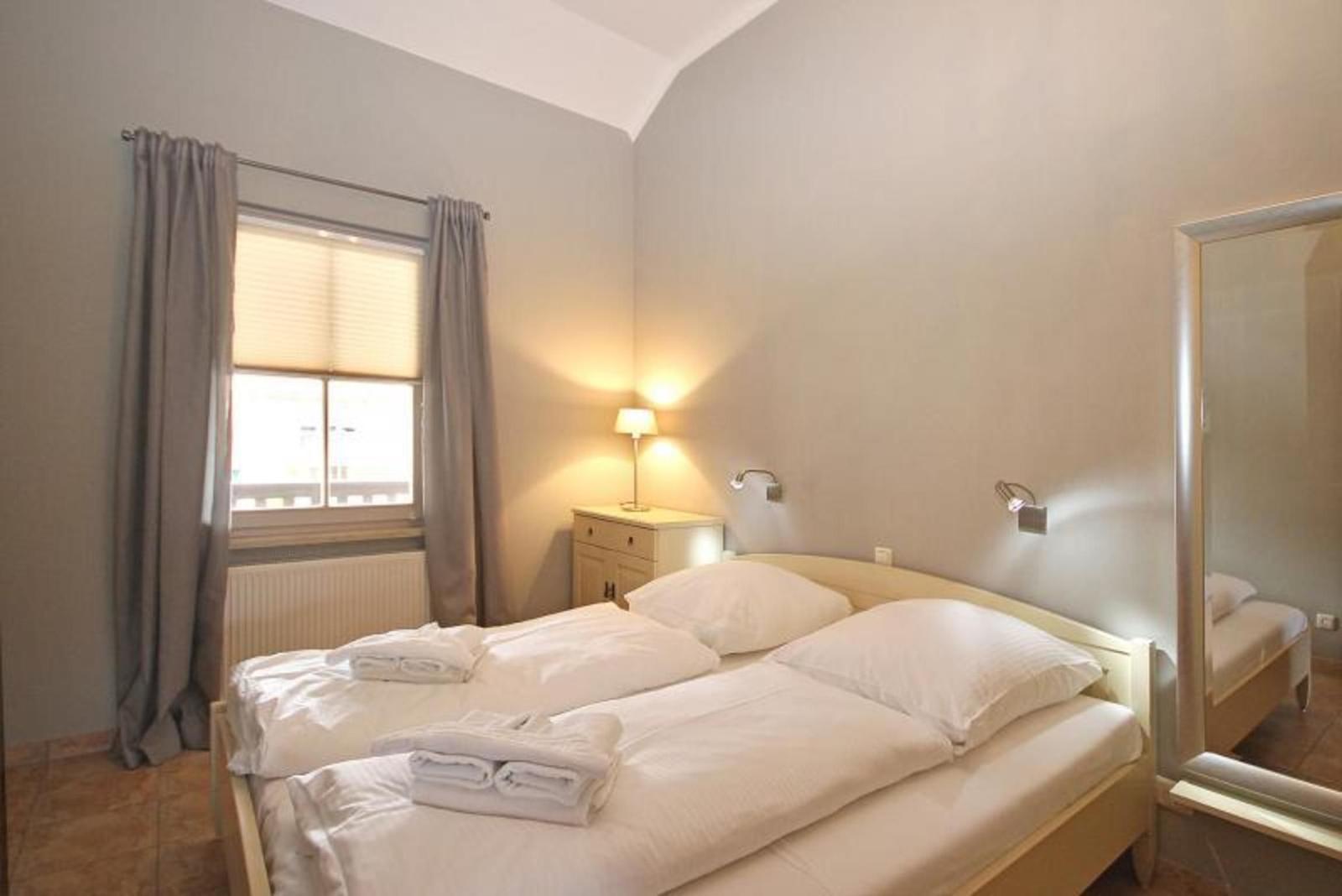 Schlafzimmer mit Doppelbett, Fenster, Spiegel und Nachttisch.