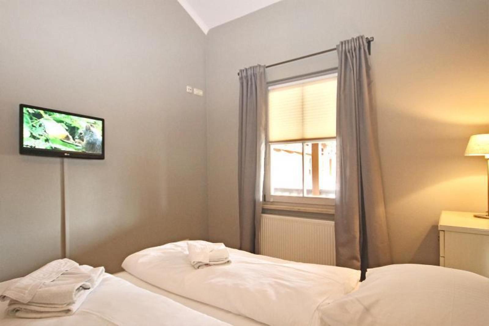 Ein Schlafzimmer mit zwei Betten, Fernseher an der Wand und Fenster mit Vorhängen.