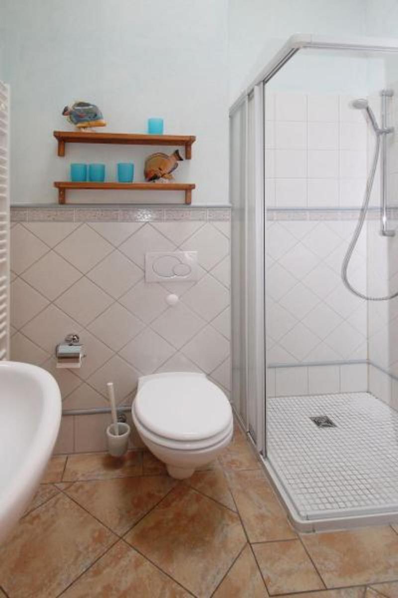 Badezimmer mit Dusche, Toilette und Waschbecken. Wandregale mit dekorativen Gegenständen.
