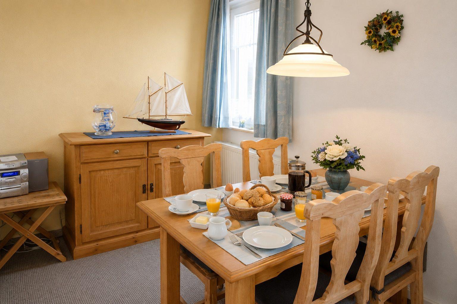 Esstisch mit Stühlen, Kaffeemaschine und Segelbootmodell auf Sideboard.