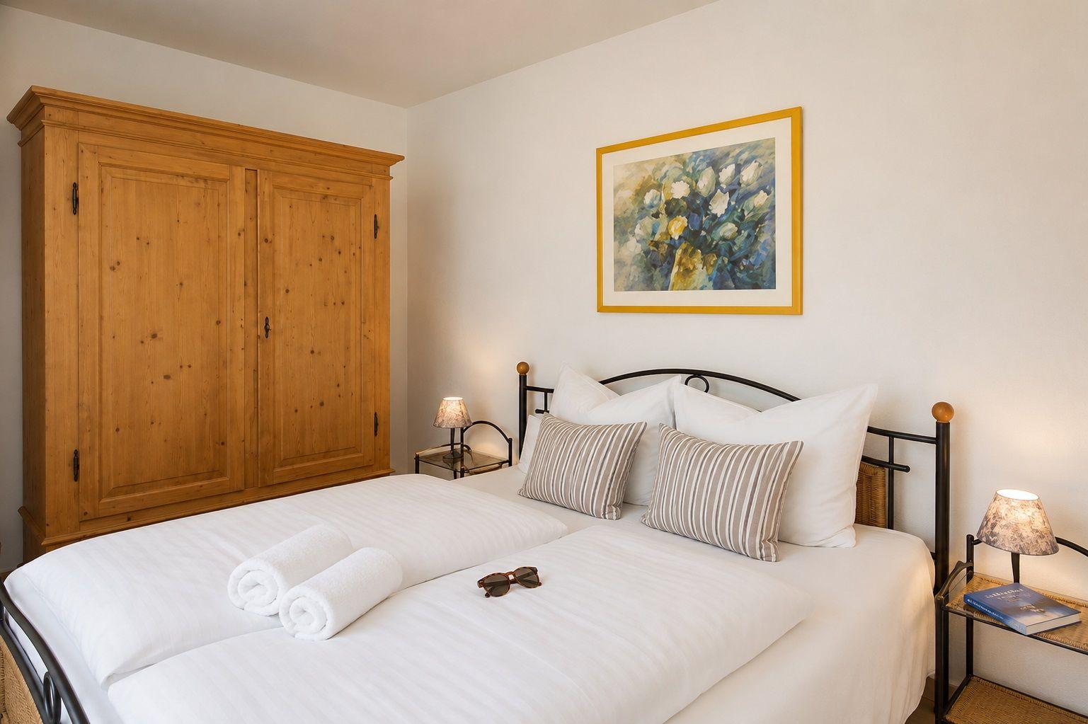 Schlafzimmer mit Doppelbett, Holzschrank und Wandbild mit Blumen.