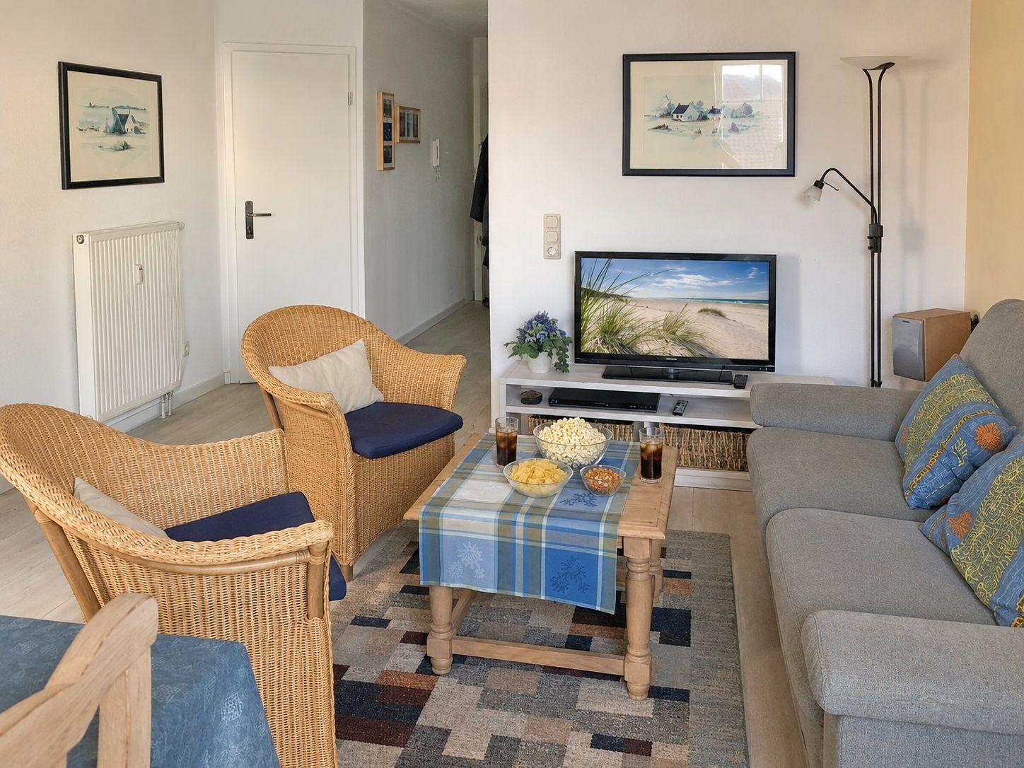 Wohnzimmer mit Sofa, zwei Rattanstühlen, Fernseher und Tisch mit Snacks.