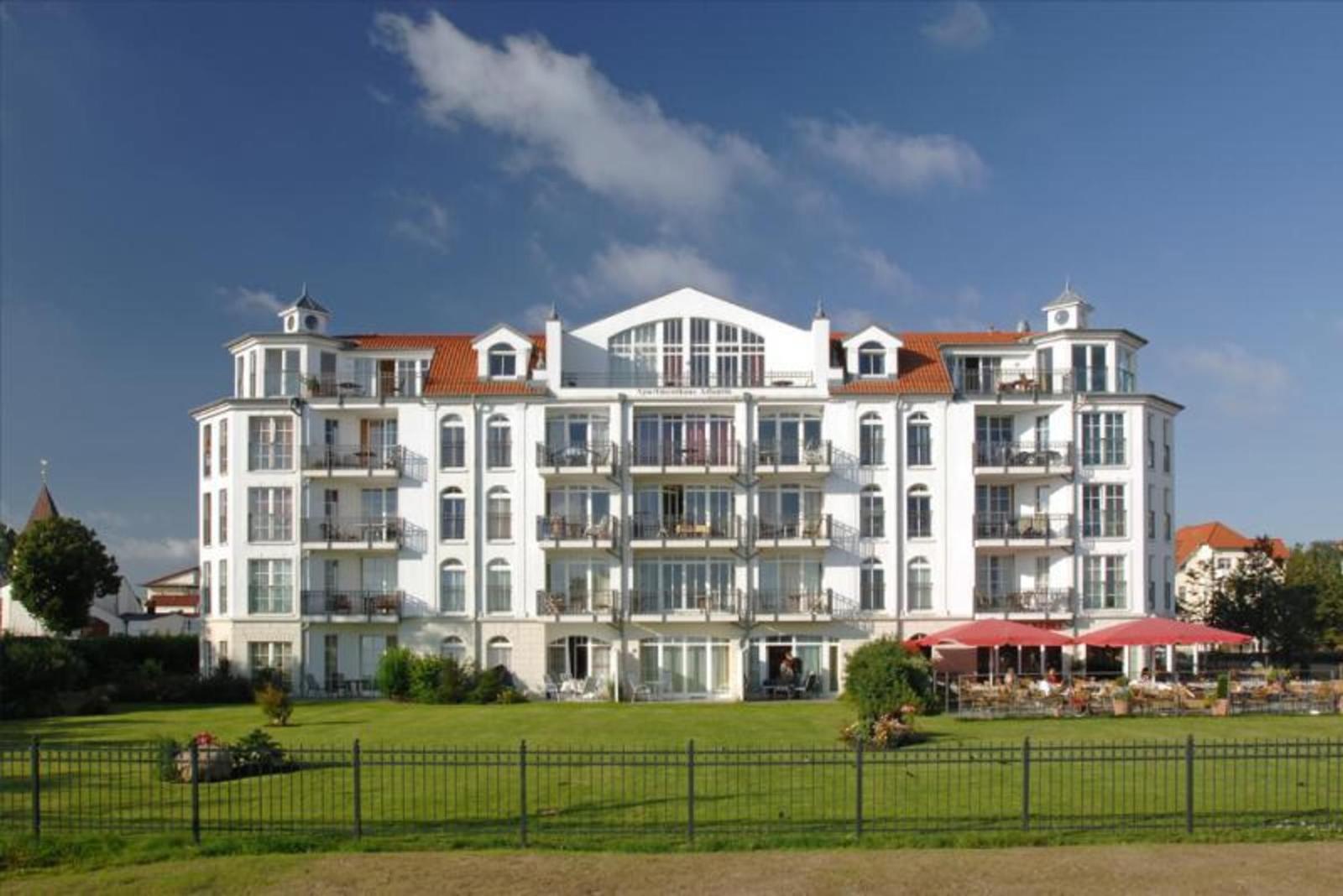Ein weißes Mehrfamilienhaus mit rotem Dach und Balkonen unter blauem Himmel.