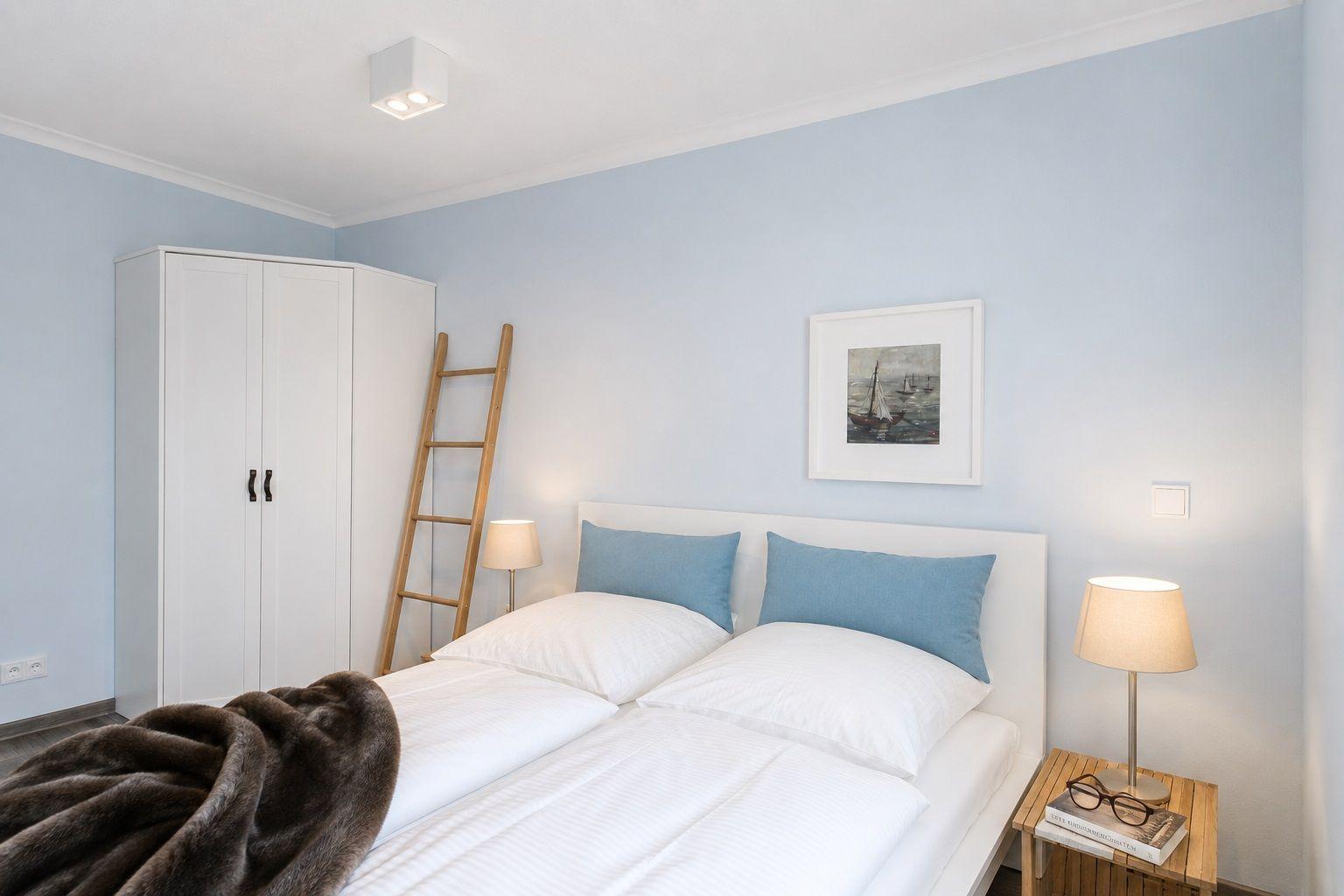 Schlafzimmer mit Bett, Nachttisch, Lampen und Kleiderschrank. Wandfarbe hellblau.