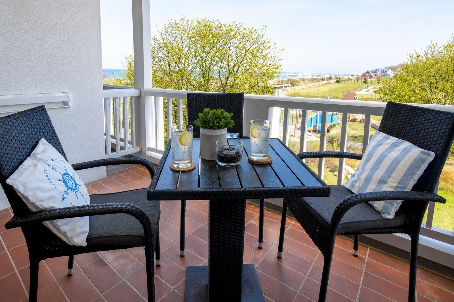 Terrasse mit Tisch und zwei Stühlen, Blick auf Grünfläche und Meer.