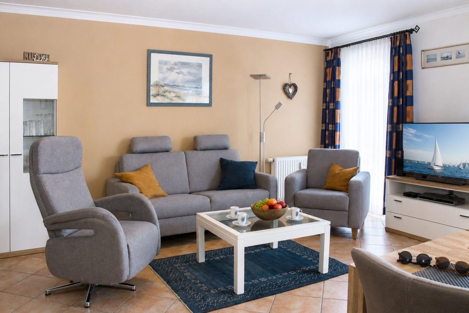 Living room with gray sofa, two chairs, glass table, and TV.