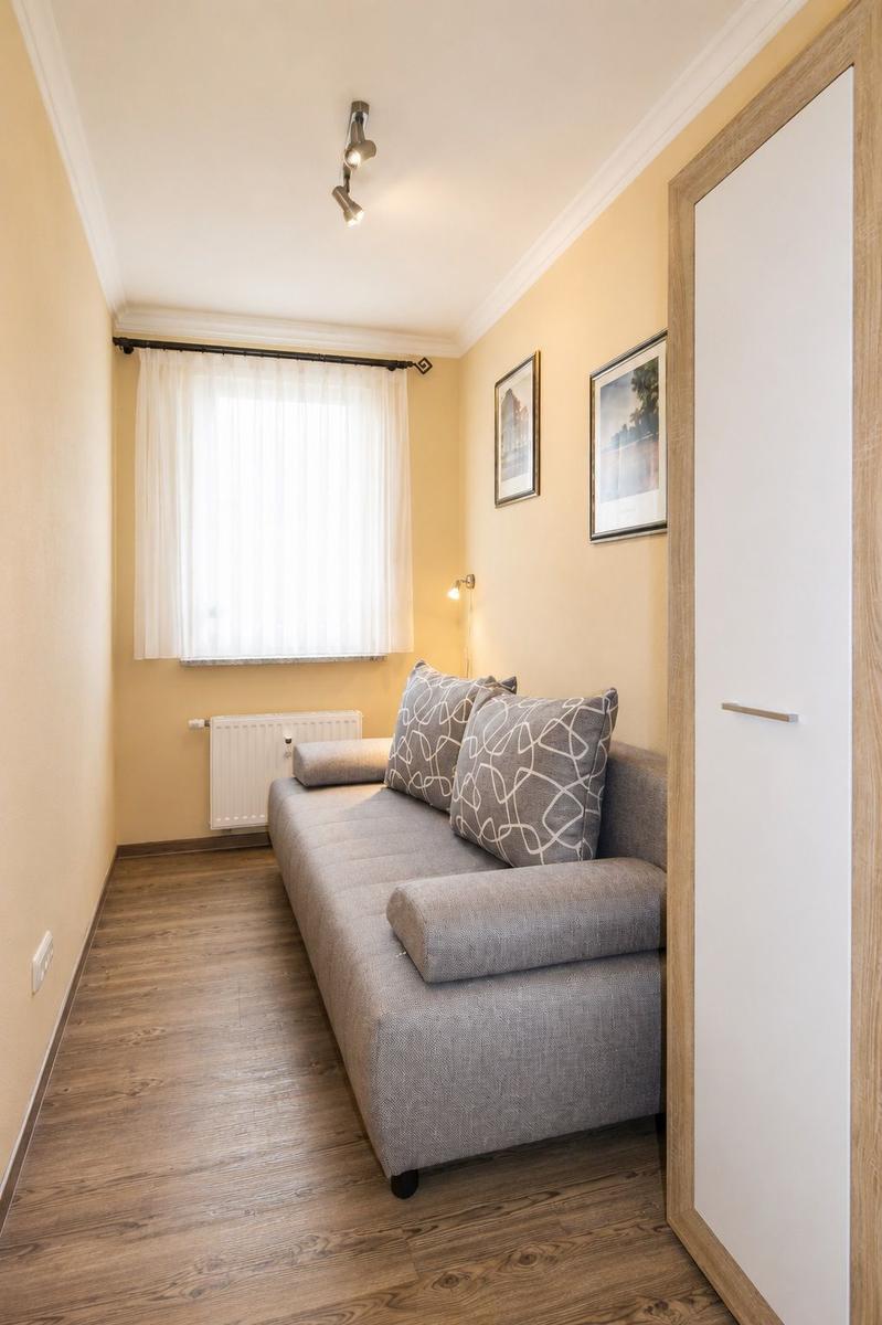 A room with gray sofa, wooden floor, and window with curtain.