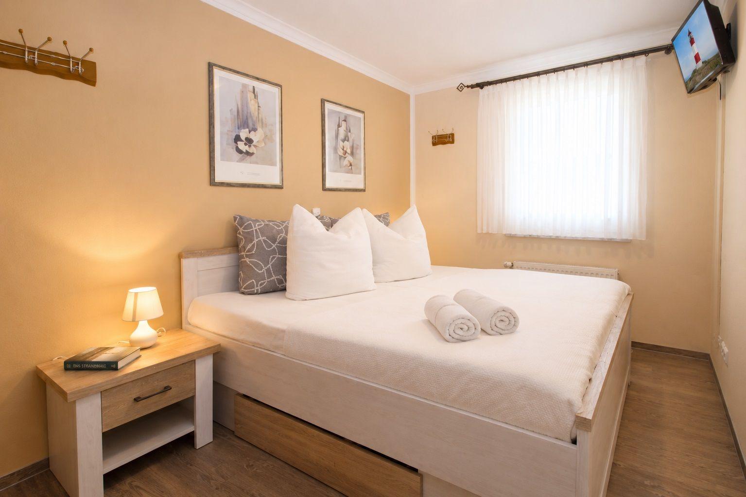 Bedroom with bed, nightstand, lamp, pictures, and TV on the wall.