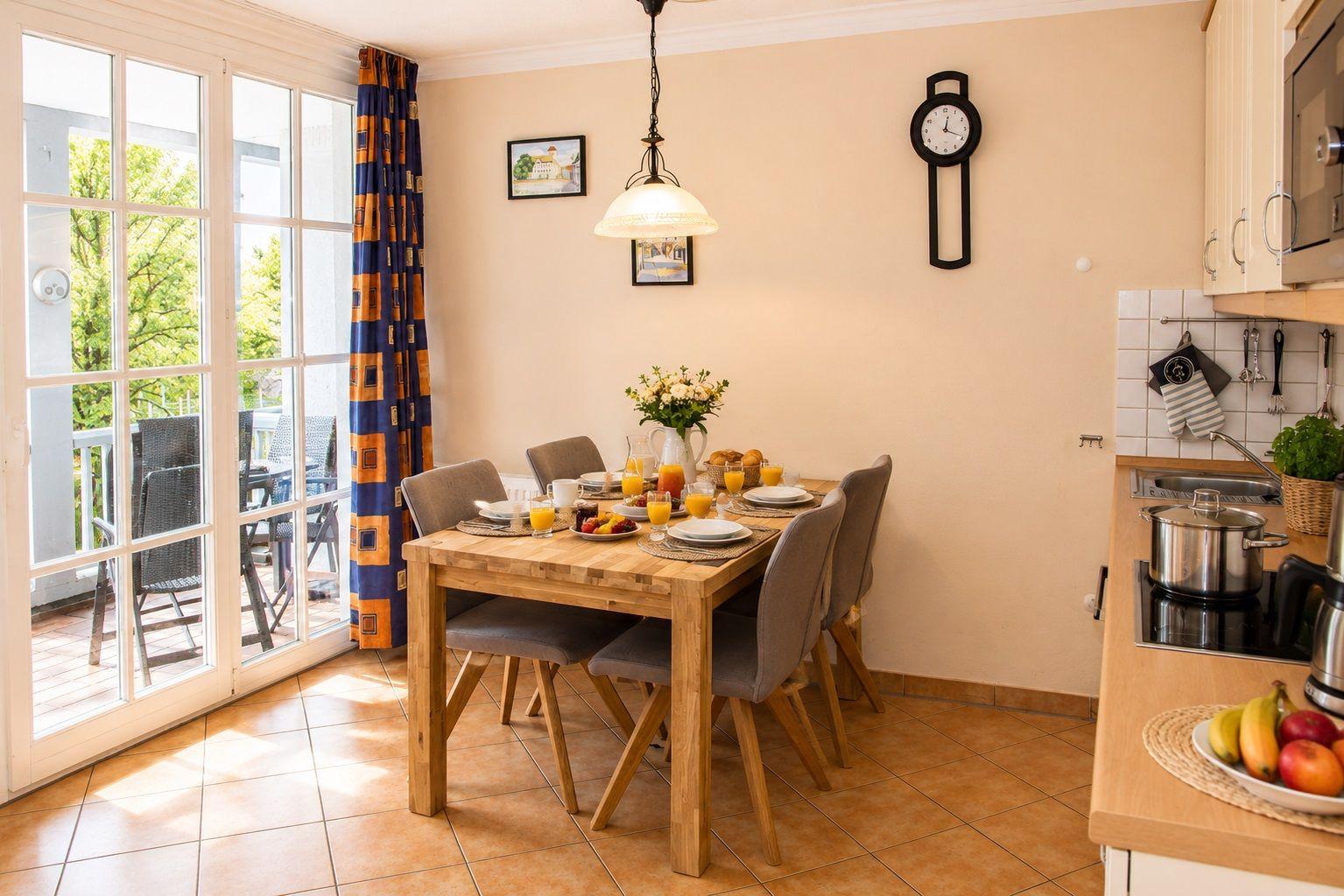 Dining room with table, chairs, and view of balcony. Kitchenette with stove and fruit.
