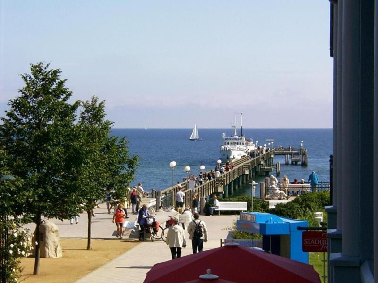 Seaside promenade with pier, boat, and pedestrians