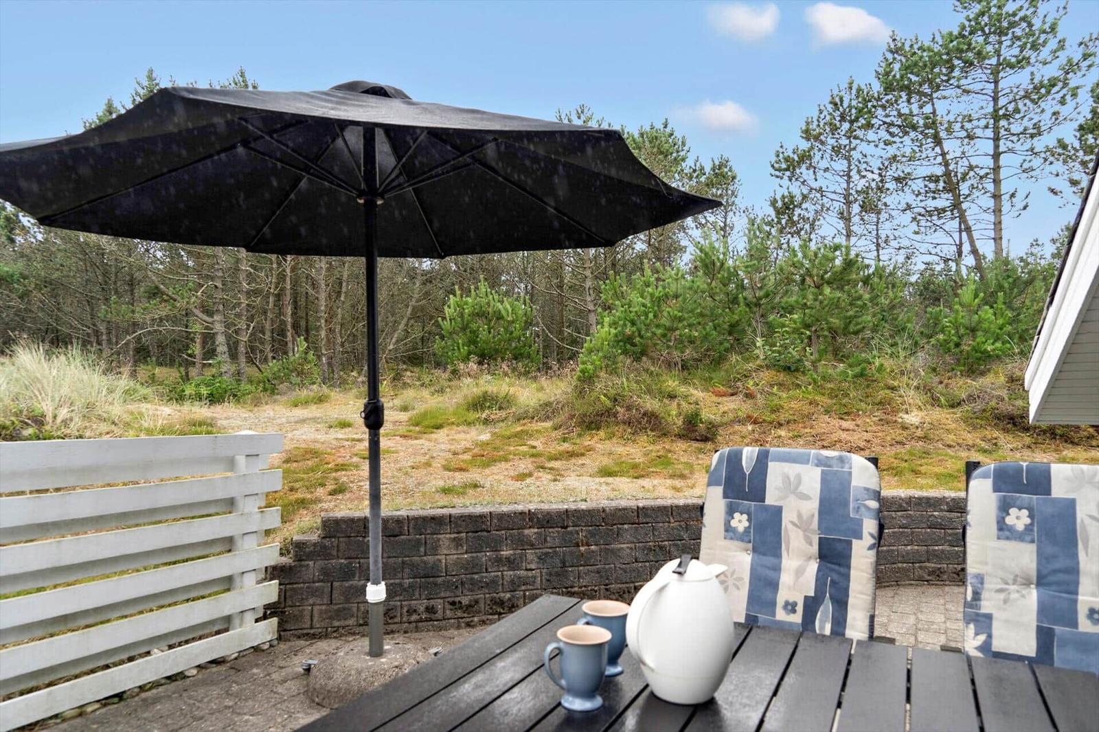 A black-clad holiday home with roof and windows. A table with chairs stands in the garden.