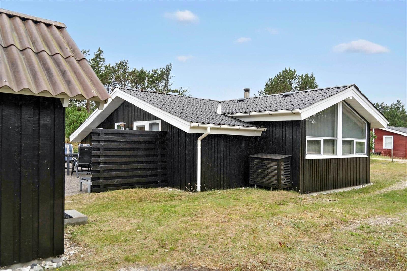 Black wooden cabin with grill and white gate in the garden.