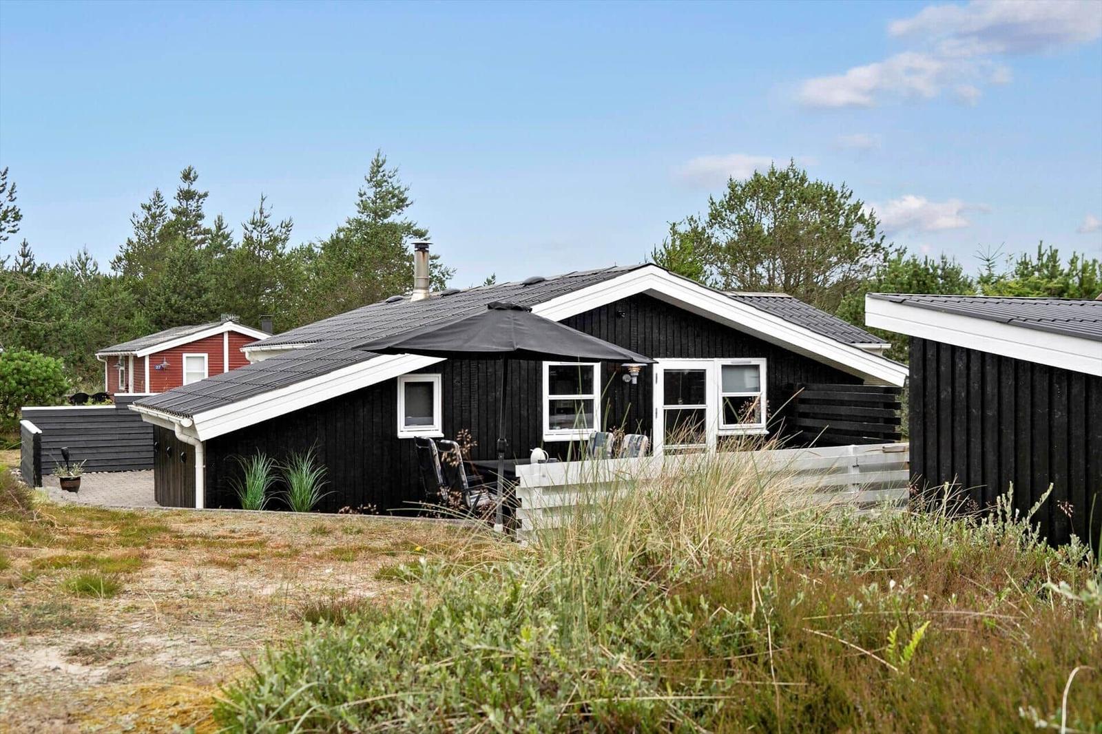 Black wooden house with terrace and garden. Surrounded by trees and grass.