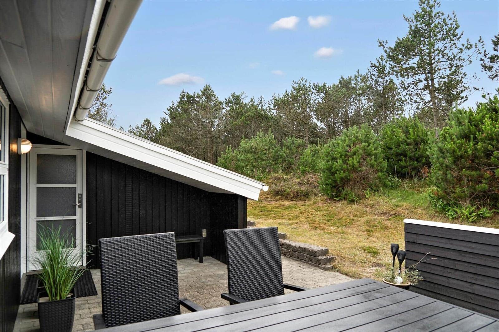 Terrace with table, chairs, and umbrella. Background: wooden house and white fence.