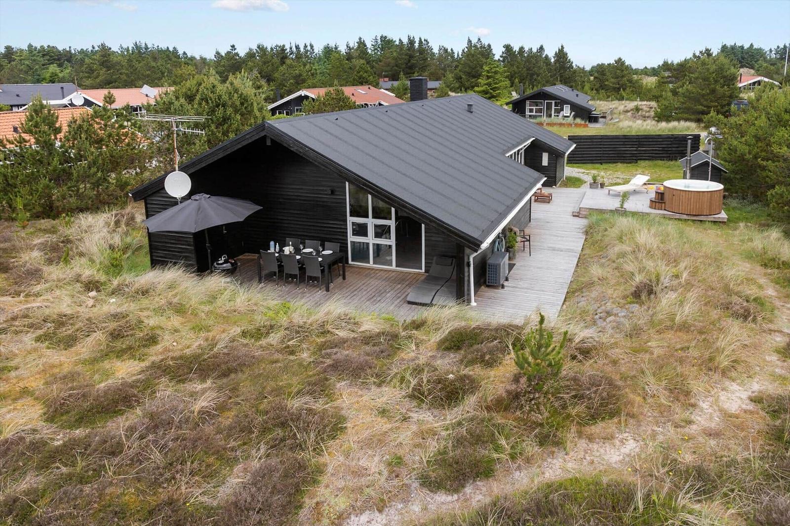 Outdoor shower with view of pine trees and wooden deck with lounge and hot tub.