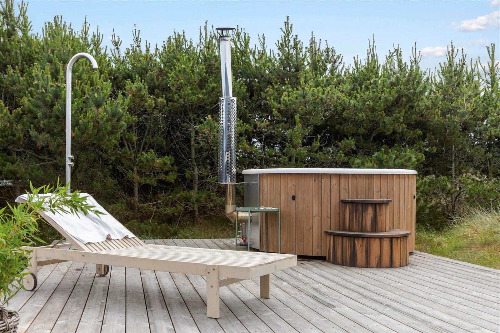 High-quality wooden hot tub on terrace with shower fixture and chimney in background.