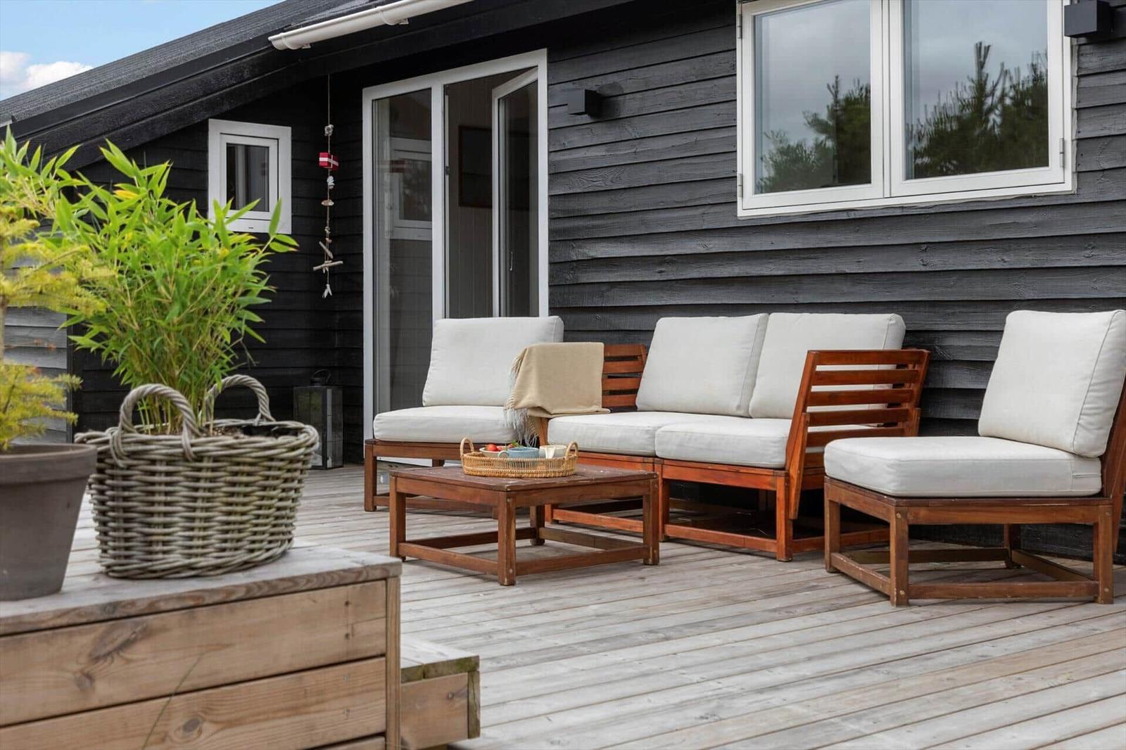 Deck with wooden furniture, seating group, and table. Dark wood wall in background.