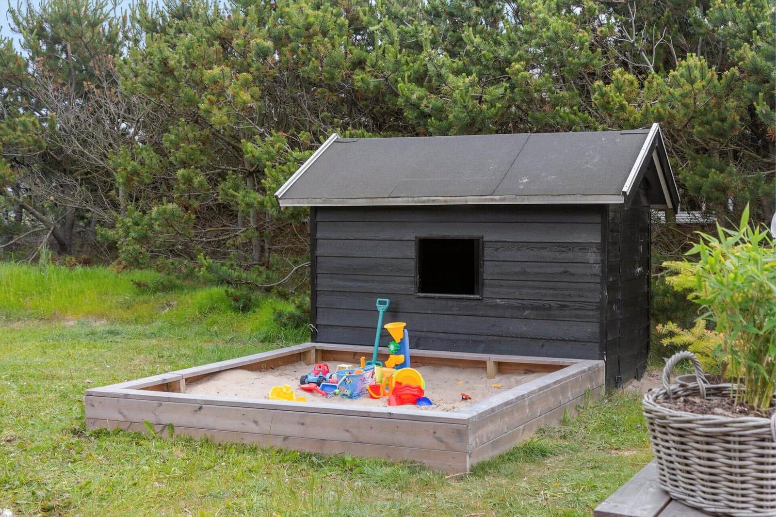 Black wooden house with terrace, grill area, and hot tub in grassland.