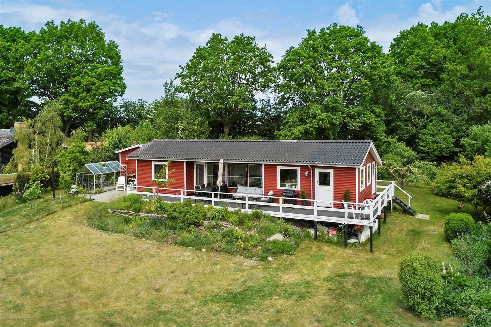 Red house with terrace, garden, and forest in the background.