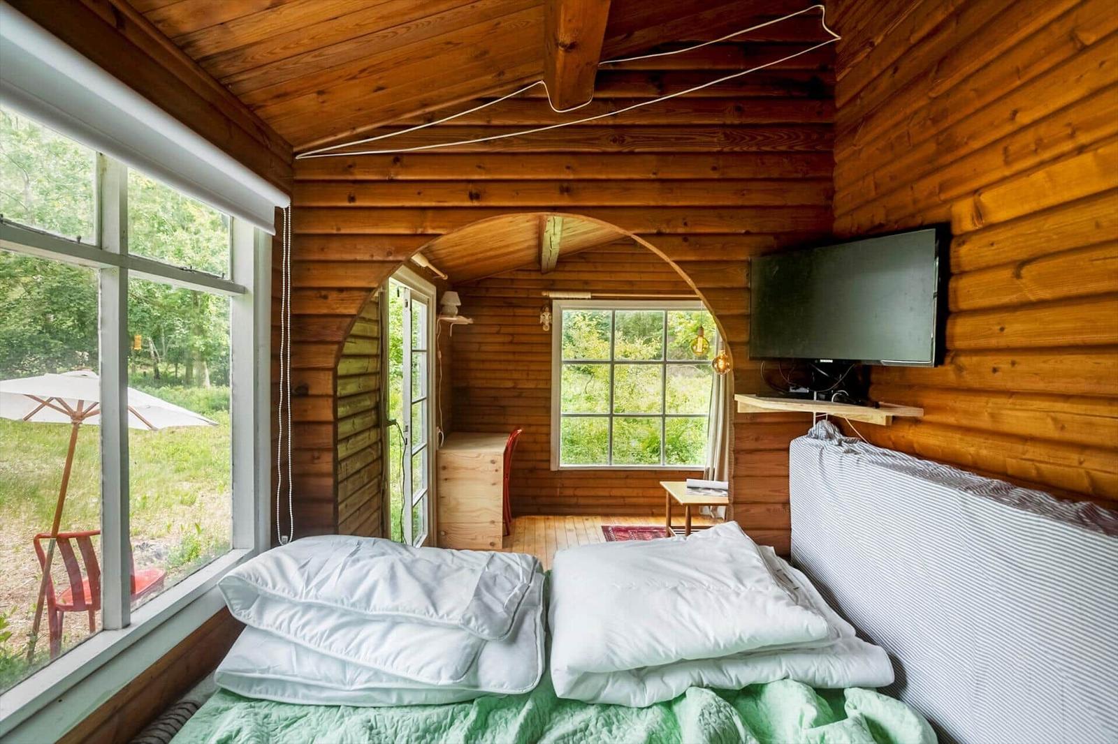 Living space with wooden walls, sofa, table, and window with view of green.