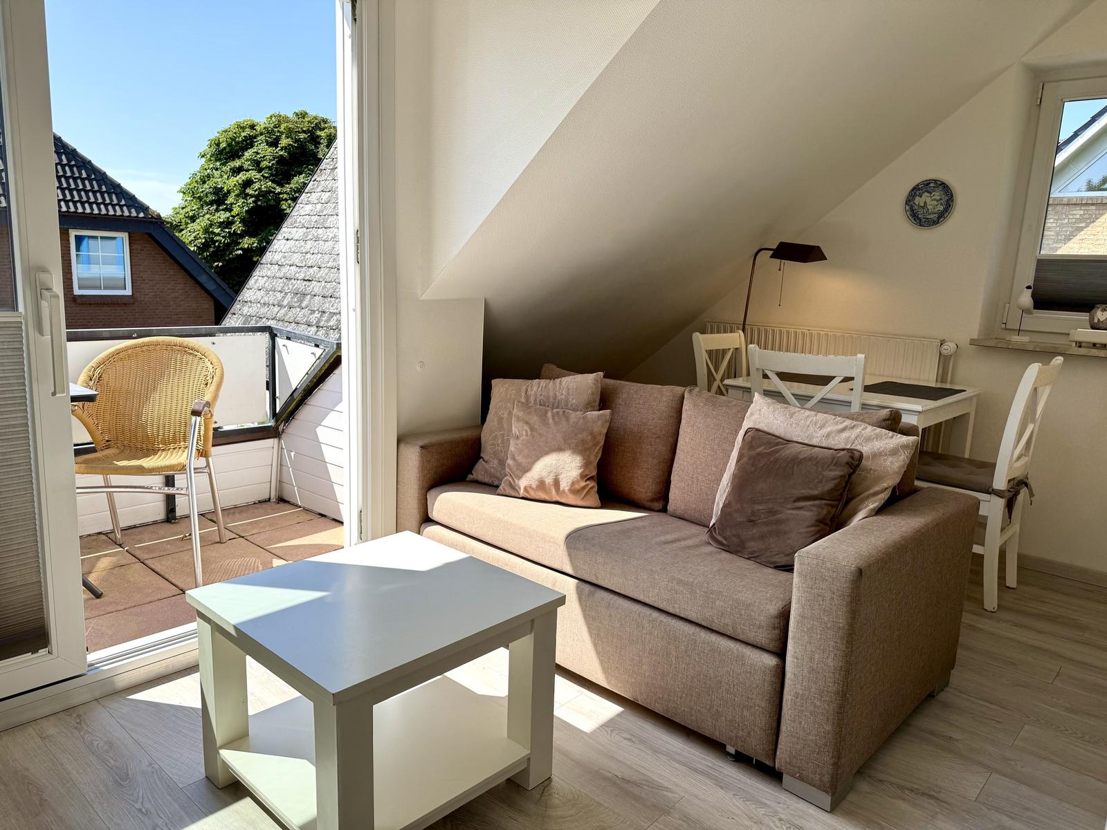 Wohnbereich mit Sofa, Couchtisch und Esstisch. Glastür zum gefliesten Balkon.