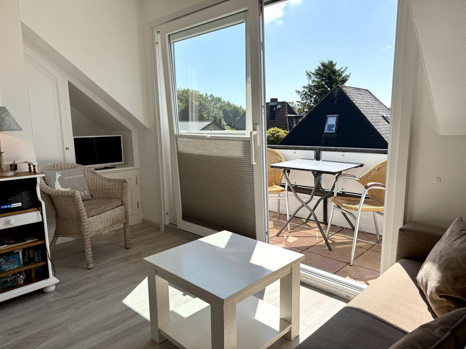 Wohnbereich mit Couchtisch, Sofa und Korbsessel. Glastür zum Balkon.
