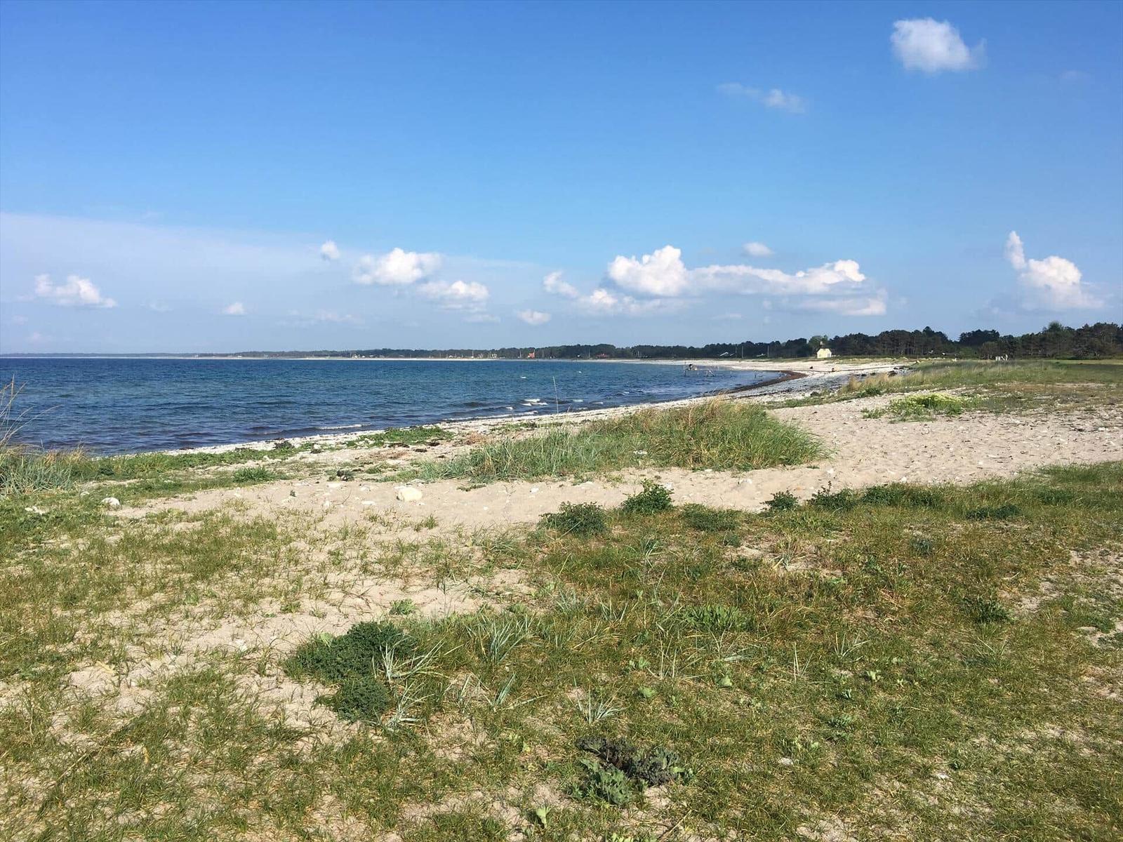 Beach with gravel shore and calm water under clear sky.
