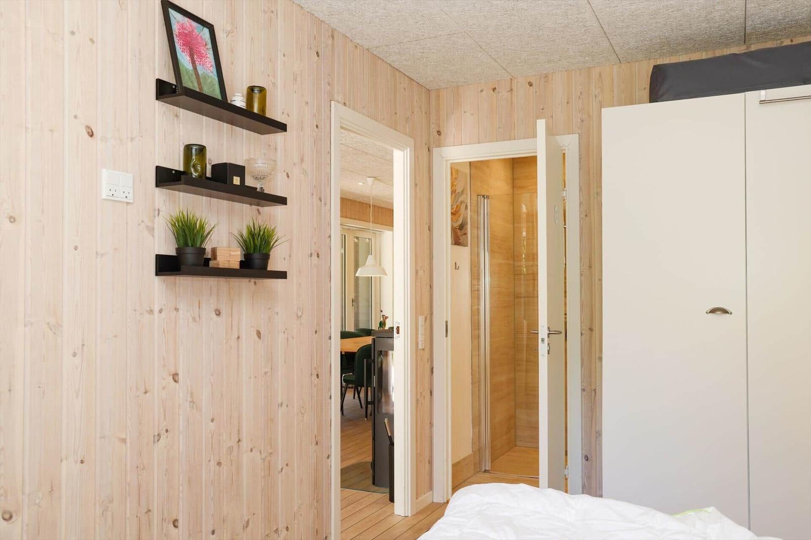 Washing machine in small room with mirror cabinet and green cushion seat.