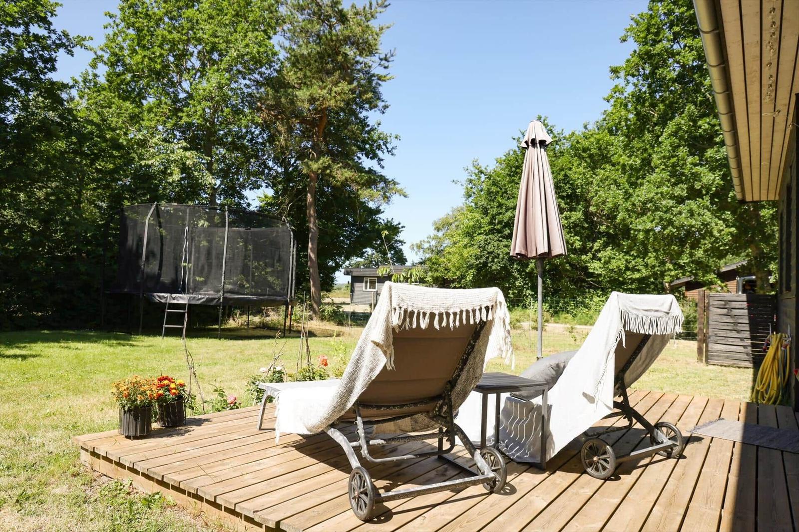 Wooden table with chairs and drinks in front of stacked firewood and trees.