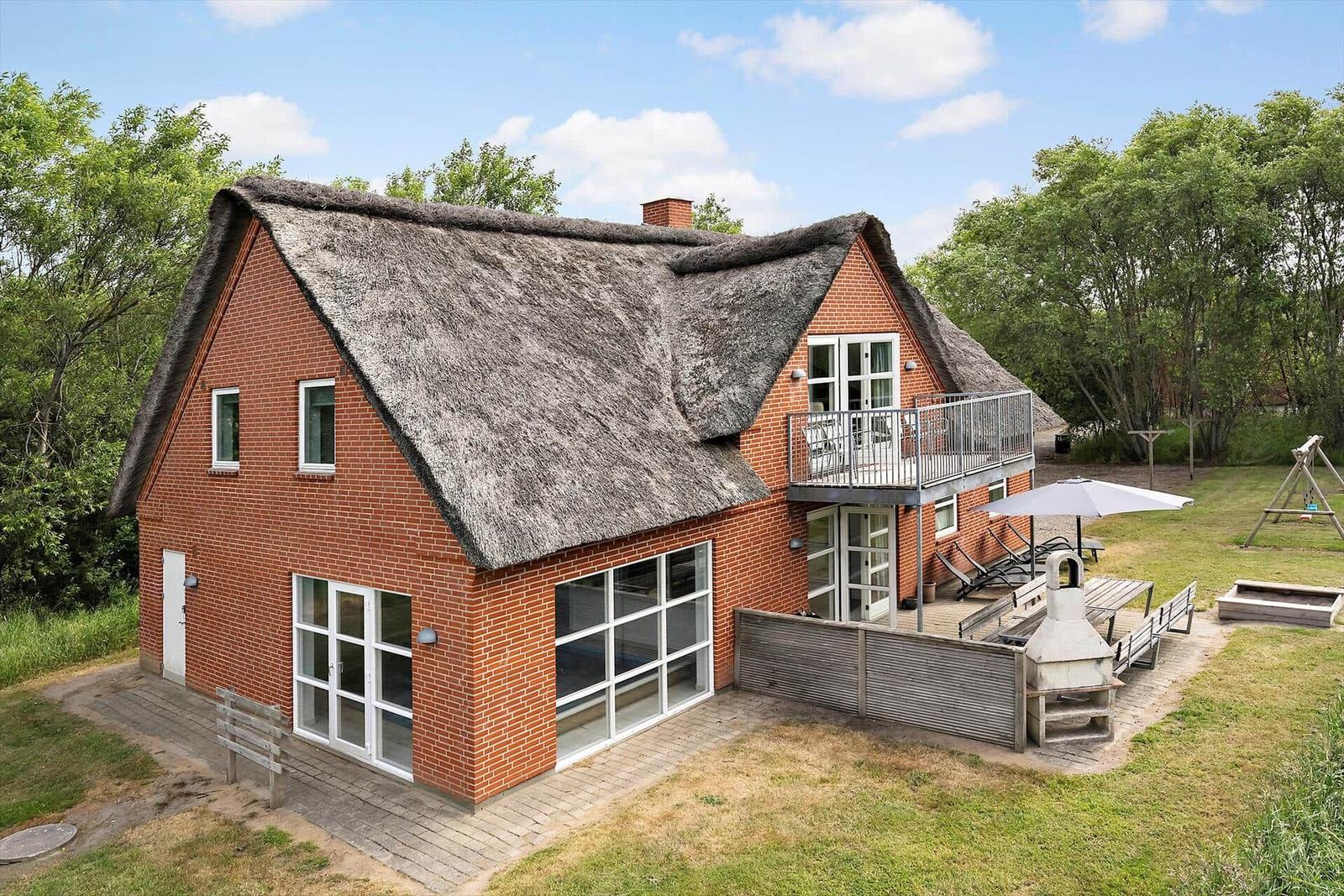 Red brick house with thatched roof and balcony. Garden area with grill and umbrella.