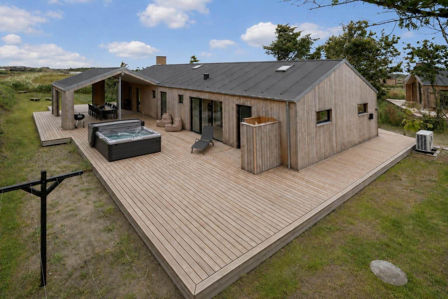 Modern wooden cabin with large deck, hot tub, and lounge area.