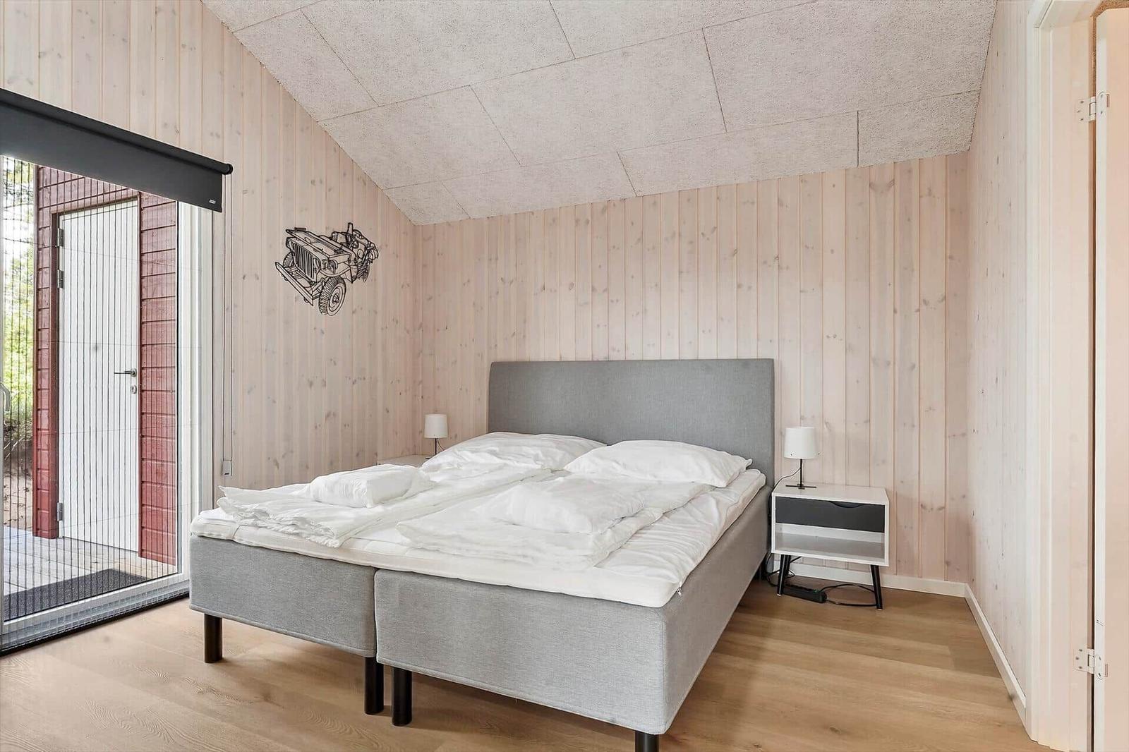 Bedroom with wooden walls, bed, and window to the forest.