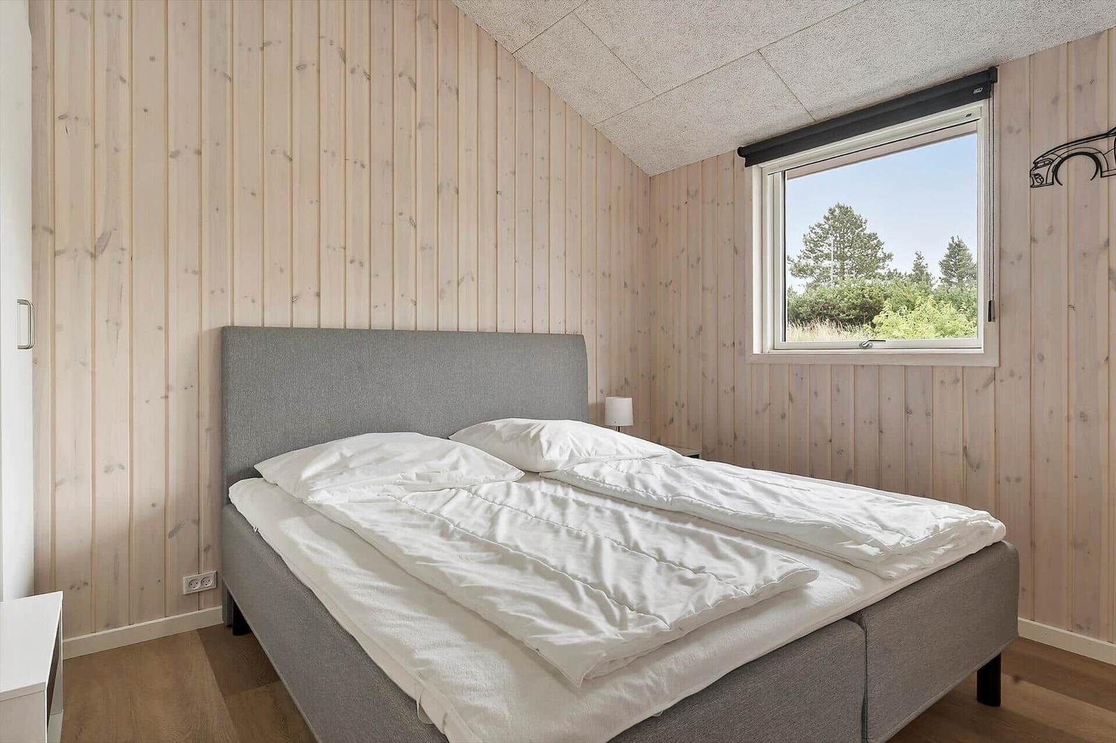 Bedroom with bed, window, and wood paneling.