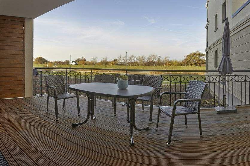 Terrasse mit Tisch und Stühlen, Blick auf grünes Feld und Wasser.