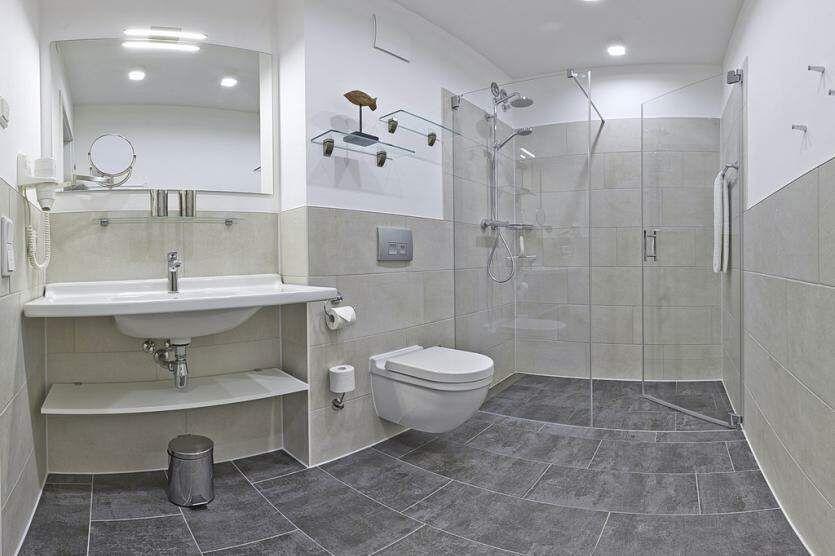 Badezimmer mit Dusche, Waschbecken und Toilette. Fliesenboden und Wandfliesen.
