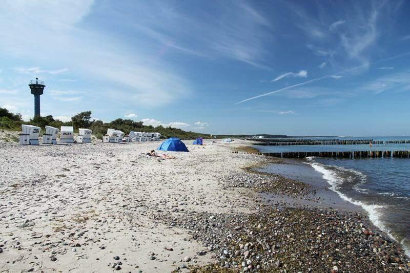 Strand mit Steinen, Strandkörben und blauem Zelt unter blauem Himmel.