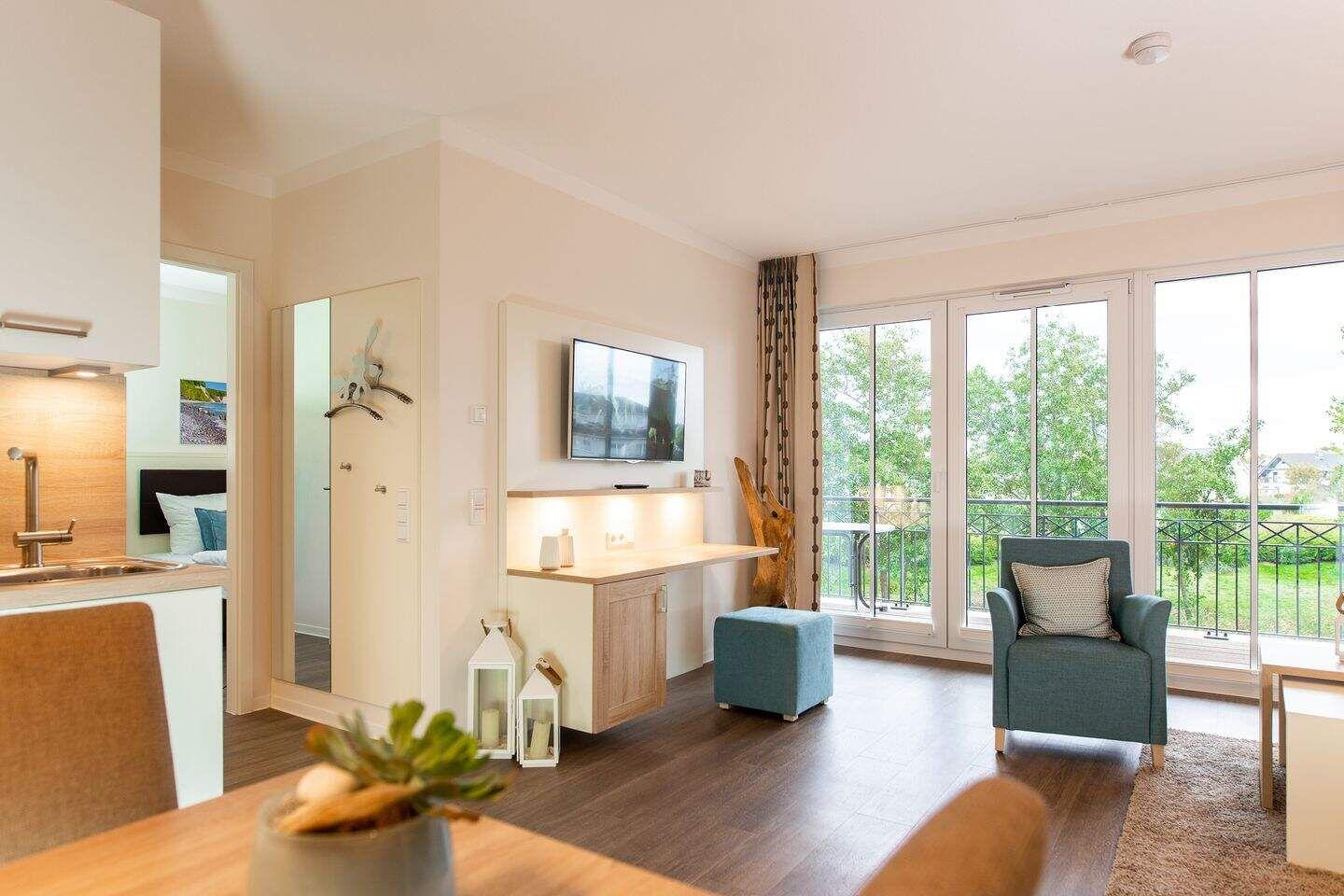 Wohnbereich mit TV, Sessel und Balkonansicht. Küche und Schlafzimmer sind sichtbar.